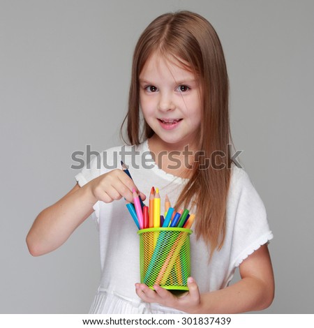 Studio image of a beautiful young caucasian girl in a white dress with colored pencils on a gray background