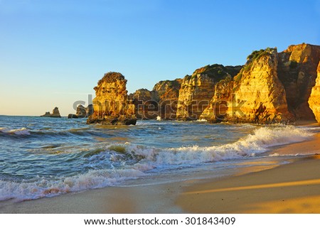 The beautiful Portuguese beach at Praia da Dona Ana at sunrise with an incoming tide, sea stacks and rocky cliffs on the coastline of the Atlantic Ocean in Lagos, Algarve, Portugal Royalty-Free Stock Photo #301843409