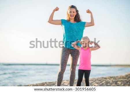 Victory... We both won the race along the water. We are like superheroes. A happy mother and daughter celebrate their victorious run along the beach at dusk, flexing their arms to show their strength. Royalty-Free Stock Photo #301956605