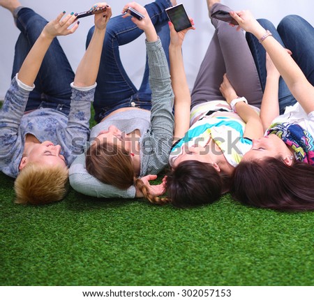 Four young women lying on green grass with mobile phone 