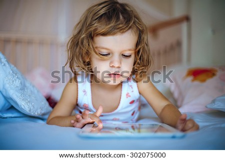 little girl playing tablet at home on a bed.