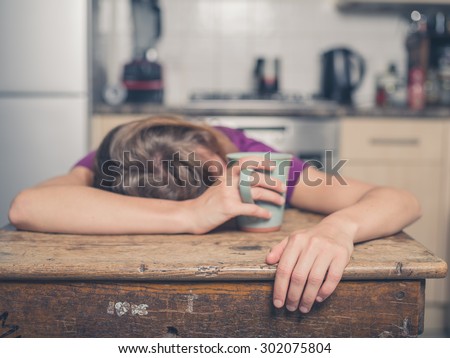 A tired young woman is having a cup of tea and is resting her head on a table Royalty-Free Stock Photo #302075804
