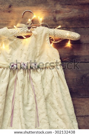 vintage cream girl's dress on hanger with on wooden background with garland lights
