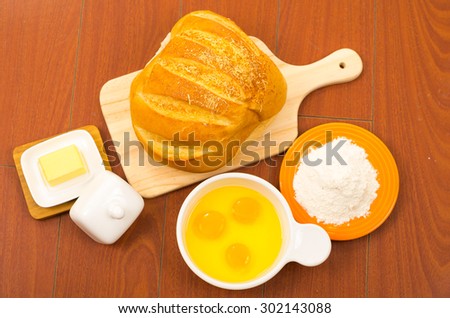 Beautifully colored loaf of bread placed on wooden surface next to white bowl with eggs, cheese and flour..