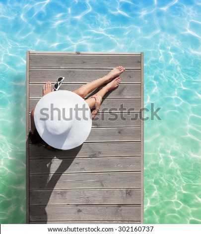 Summer holiday fashion concept - tanning woman wearing sun hat at the pool on a wooden pier view from above