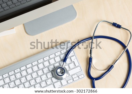 Medicine doctor's working table view from top. Monitor, keyboard, mouse and stethoscope lying on table at physician's office. Medical concept