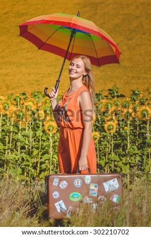 Picture of female holding rainbow umbrella and travel suitcase on the sunflower field outdoors background copy space