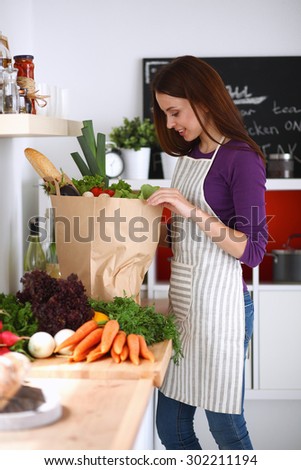 Young woman standing in her kitchen near desk with  grocery shopping bags