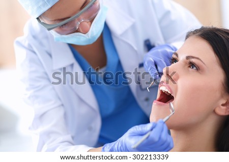 Woman dentist working at her patients teeth Royalty-Free Stock Photo #302213339