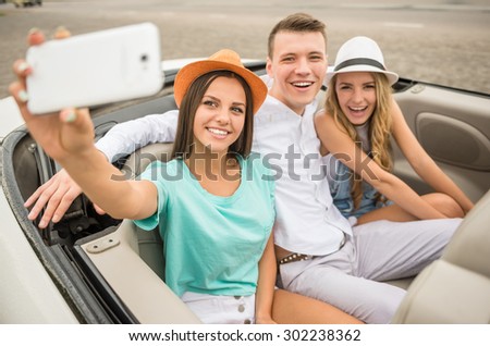 Three beautiful friends taking selfie while sitting in the cabriolet on rear seats.