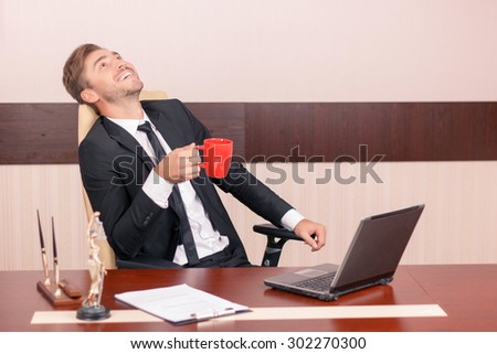 Time to relax. Upbeat handsome lawyer sitting at the table and drinking tea while having rest