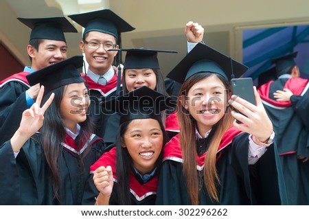 Asian university graduates taking photo with handphone