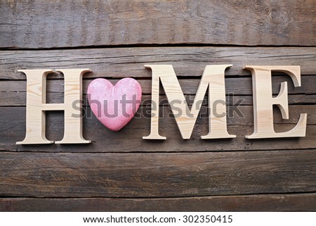 Decorative letters forming word HOME with heart on wooden background