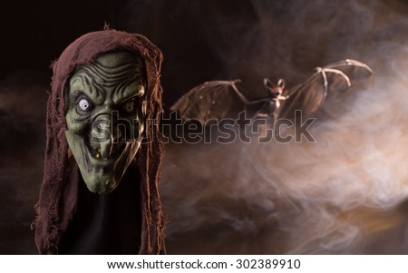 Scary halloween witch head and a flying bat on a background of swirling smoke