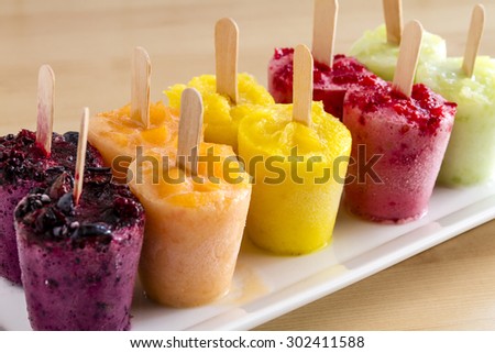 Assorted flavors of homemade fresh pureed frozen fruit popsicles sitting on white plate in a row Royalty-Free Stock Photo #302411588