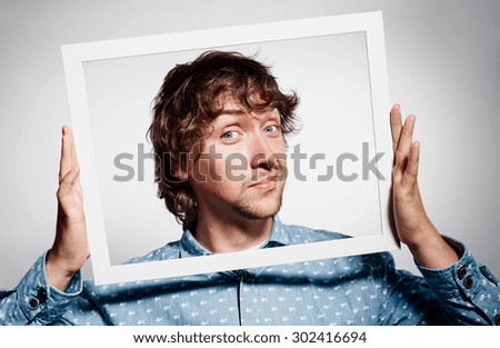 Closeup portrait businessman executive looking at camera, curious surprised confused through white picture frame thinking beyond borders accepted rules isolated grey background.Face expression emotion