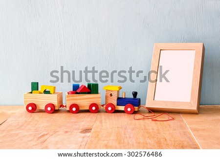 Wooden toy train over wooden table next to photo blank frame