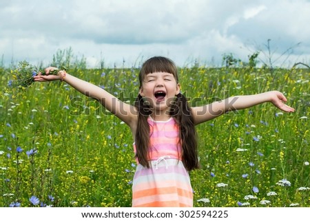 Cheerful little girl happy and fun screaming in a meadow among the flowers