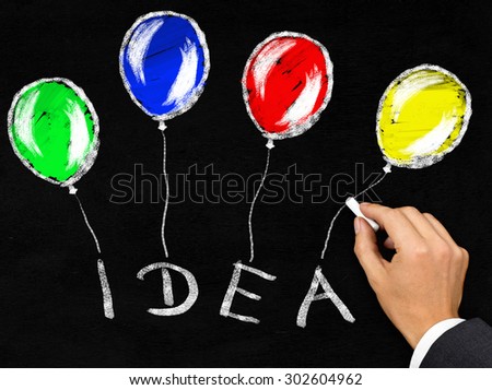 Man writing the word 'Idea' with balloons attached to it with chalk on blackboard background