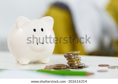 Pile of different coins near white piggybank on table closeup. Budgeting expenses concept. Making savings and effective investment concept. Future needs deposit