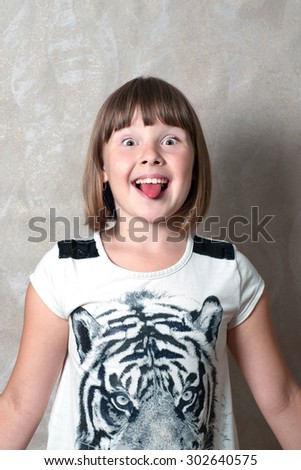 Happy teen girl poses a face near grey wall