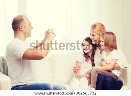 family, children, photography and home concept - smiling happy father taking picture of mother and two daughters at home