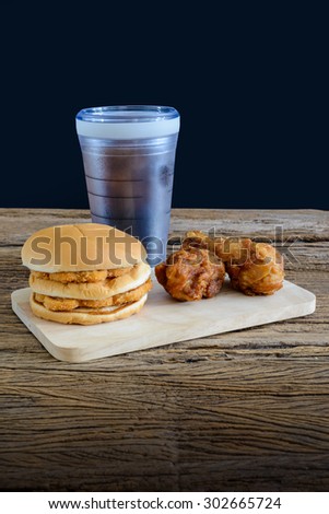 chicken hamburger and fried chicken, glass of cola on wooden cutting board on top wooden table
