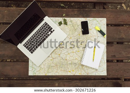 Planning travel on wood table outside with map, laptop, knife, notebook and pen