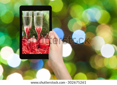 man takes photo of Christmas still life - Two glasses of sparkling wine with red Xmas baubles and tinsel on green blurred Christmas tree background