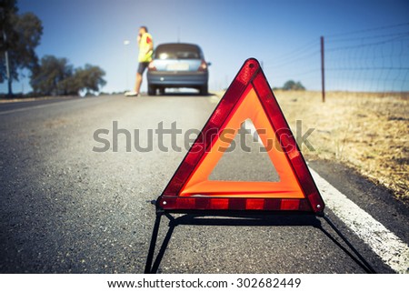 Emergency triangle on the road, stopped car and man calling by phone in the background.