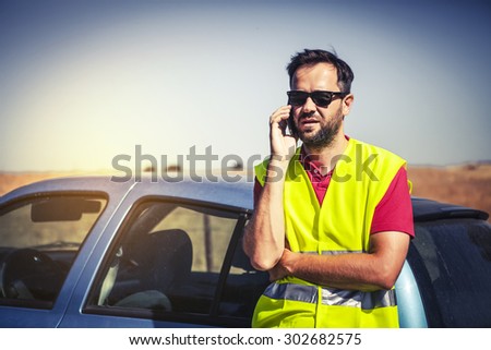 Man with a reflective vest calling to insurance company after a car failure.