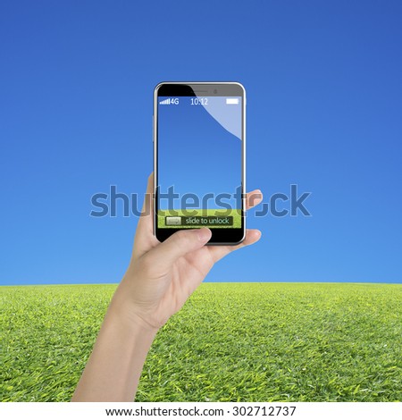 Woman hand holding smart phone, with thumb pushing button, front view, on blue sky and grass background.