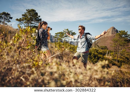 Young man hiking and posing for girlfriend with a camera who is taking his picture. Hikers enjoying in nature. Young couple on summer vacation in countryside.