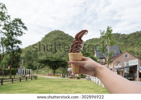 Hand holding ice cream with farm background.