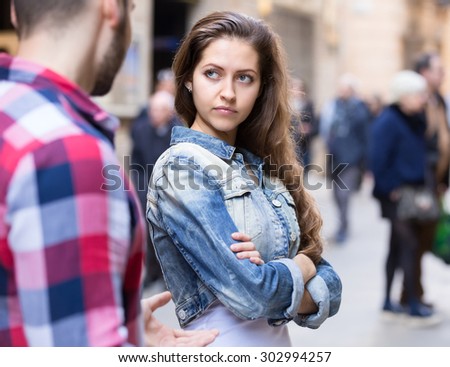 Couple having a quarrel on a city street. Woman is standing half-turned to her boyfriend with a dissapointed look on her beautiful face Royalty-Free Stock Photo #302994257