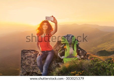 Young woman hiking in the mountains and taking a picture of herself on smartphone