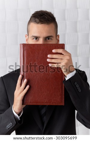 Smiling businessman with brown eyes hiding behind the deep red register. Man with short hair in business suit is real professional in his sphere.