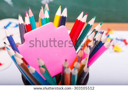 Colorful pencils of red yellow orange violet purple pink green and blue and stick on school desk with white sheet of paper on written with chalk blackboard background copyspace, horizontal picture