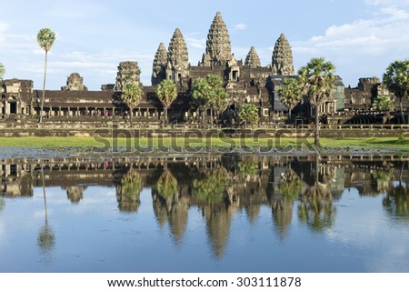 Ancient temple complex of Angkor Wat reflecting in still water under blue sky