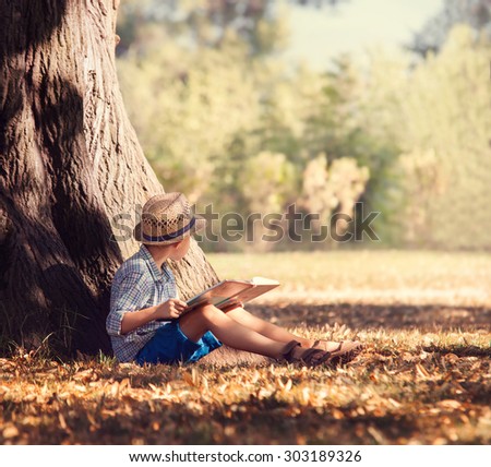 Boy with book siting under the big tree in sunny afternoon