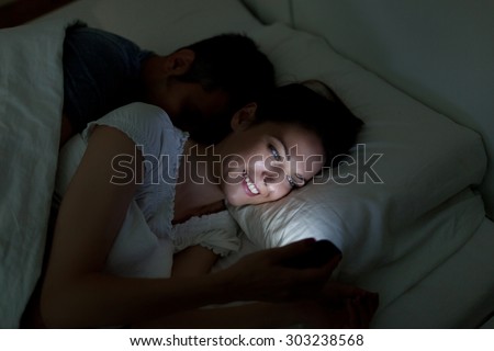 Young woman using mobile phone, while husband asleep Royalty-Free Stock Photo #303238568