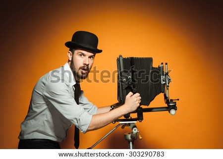 side view of young  afraid man in hat as photographer with retro camera on an orange background