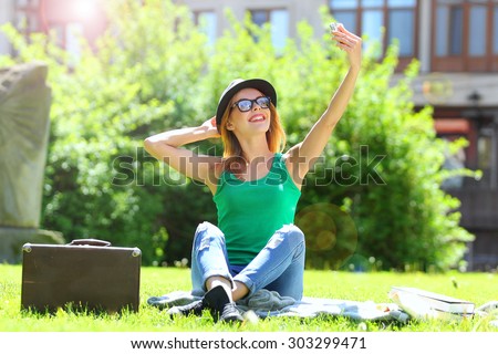 Young beautiful woman in the park, sitting on green grass, takes pictures self.