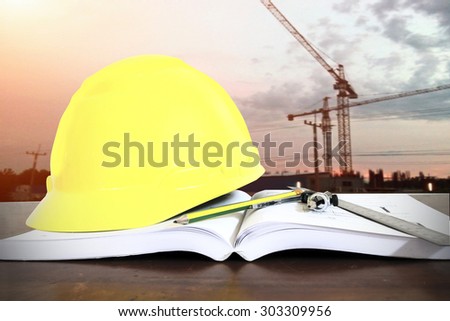 hard hat with pencil compasses and rulers/book on table at construction site background