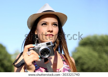 beautiful brown hair girl with white panama hat holding her camera and walking at park in a sunny day. summer portrait  