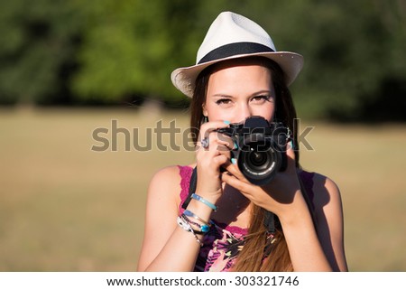 beautiful brown hair girl with white panama hat while shooting a picture with her camera at park in a sunny day. summer portrait   Royalty-Free Stock Photo #303321746