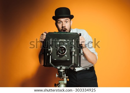 Young  afraid man in hat as photographer with retro camera on an orange background