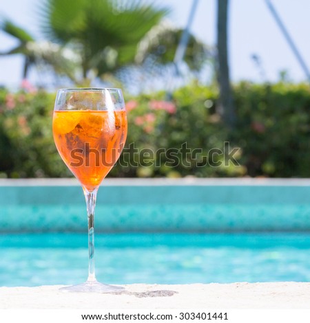 Glass of Aperol Spritz cocktail on the pool nosing at the tropical resort. Square, cocktail on left side