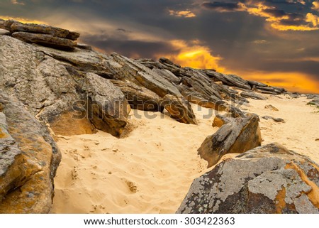 Stone desert. Old rocks on yellow sand on  fantastic sunset background . Orange clouds illuminated by sun.