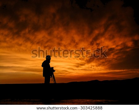 Photographer with camera on tripod silhouette at sunset